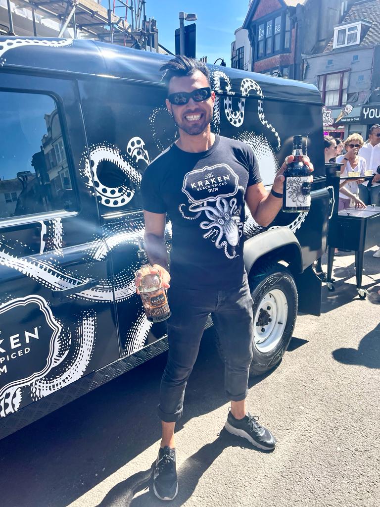 Kraken rep holding Kraken rum in front of black Land Rover Defender